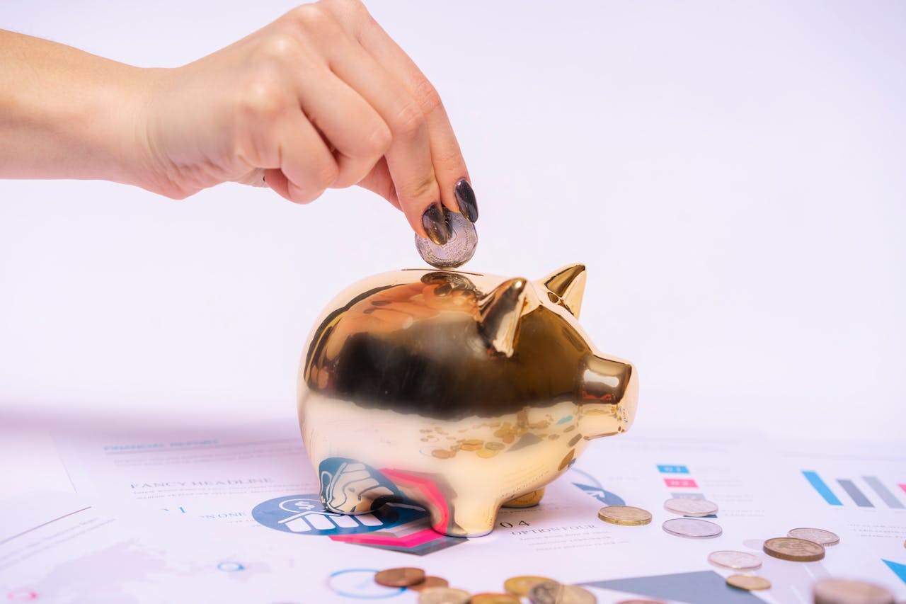 portfolio-01 A hand places a coin into a golden piggy bank surrounded by financial documents, symbolizing savings.